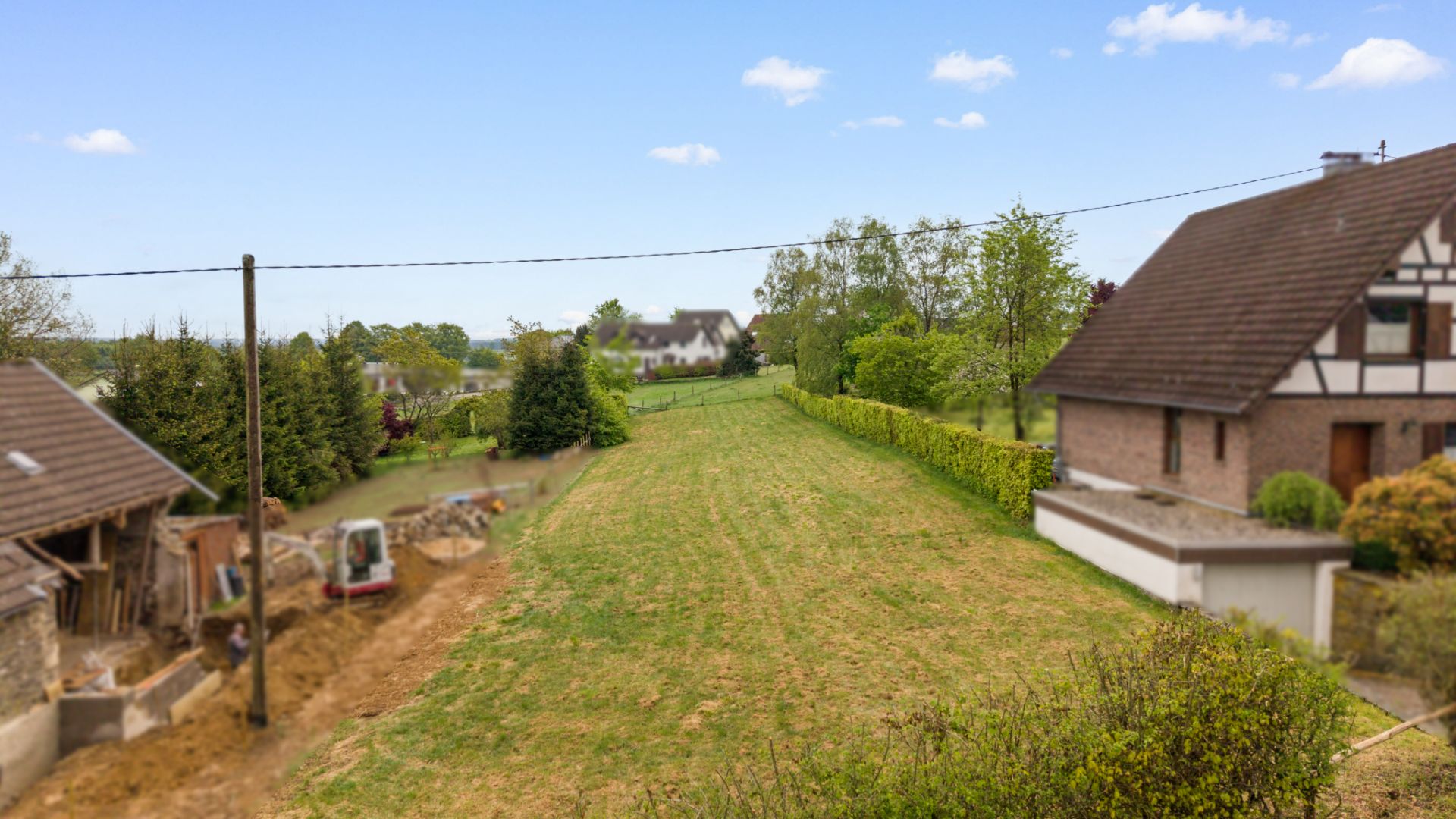 Großer, rechteckiger Garten zwischen zwei Wohnhäusern mit Rasen und einigen Bäumen im Hintergrund.