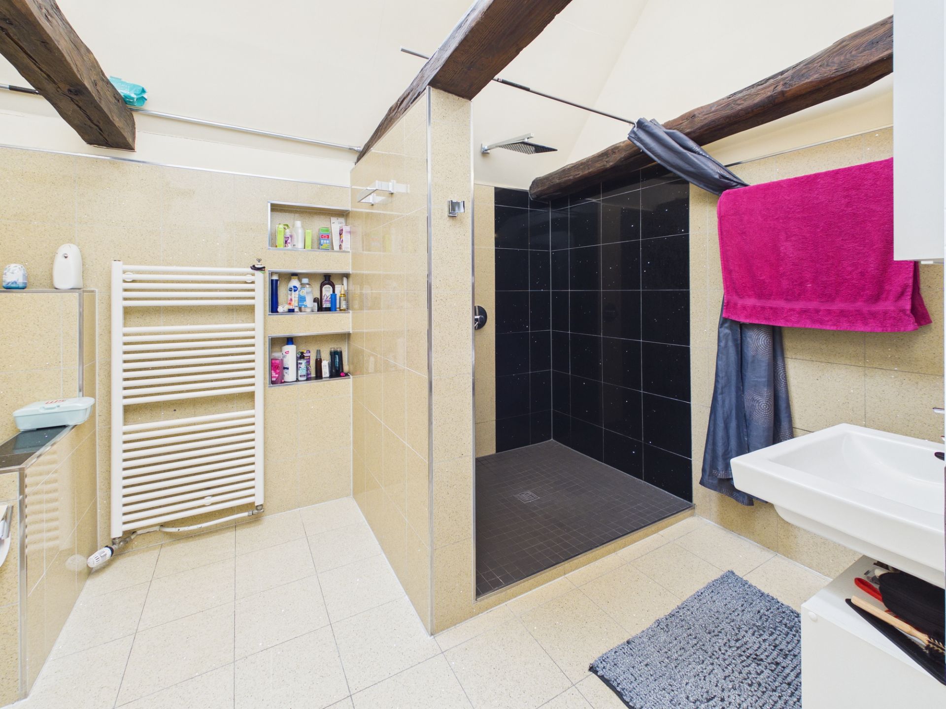 Modernes Badezimmer mit großer begehbarer Dusche, Handtuchheizkörper und Regal mit Pflegeprodukten.