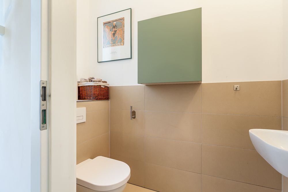 Modernes WC mit beigem Fliesenspiegel, grünem Wandschrank und kleinem Waschbecken.