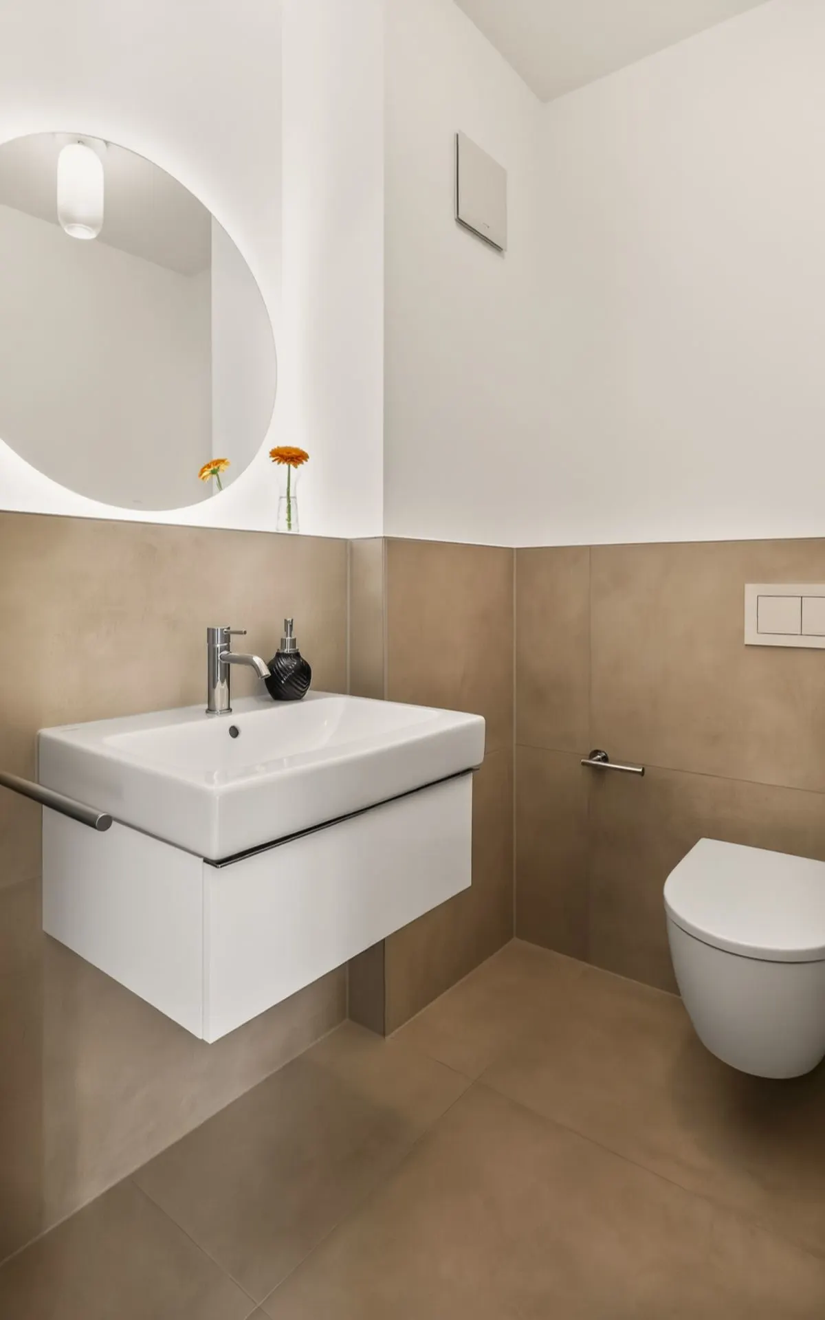 Modernes Badezimmer mit Hängewaschbecken, rundem Spiegel und Wandtoilette.