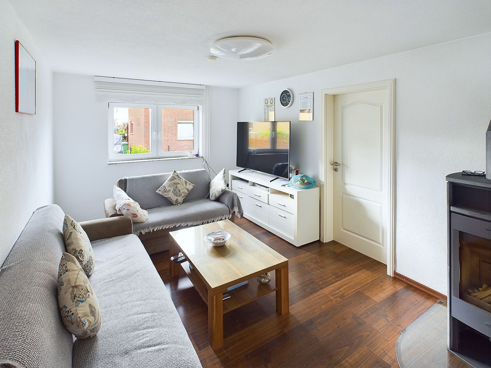 Helles Wohnzimmer mit zwei Sofas, Couchtisch, Fernseher auf Sideboard und Kaminofen.