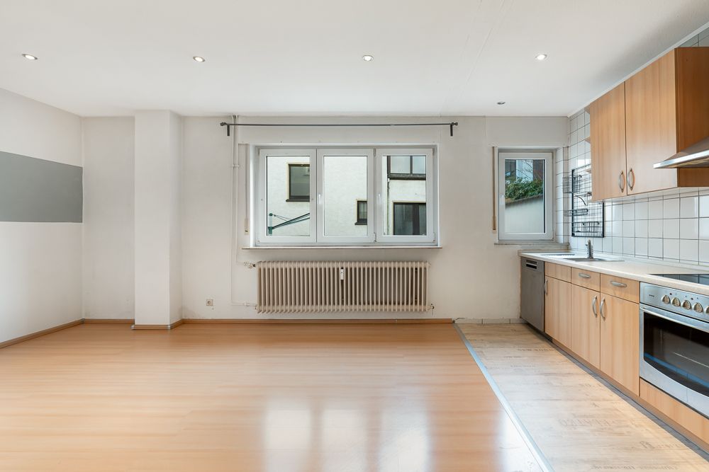 Helles Wohnzimmer mit offener Einbauküche, großen Fenstern und Holzboden.