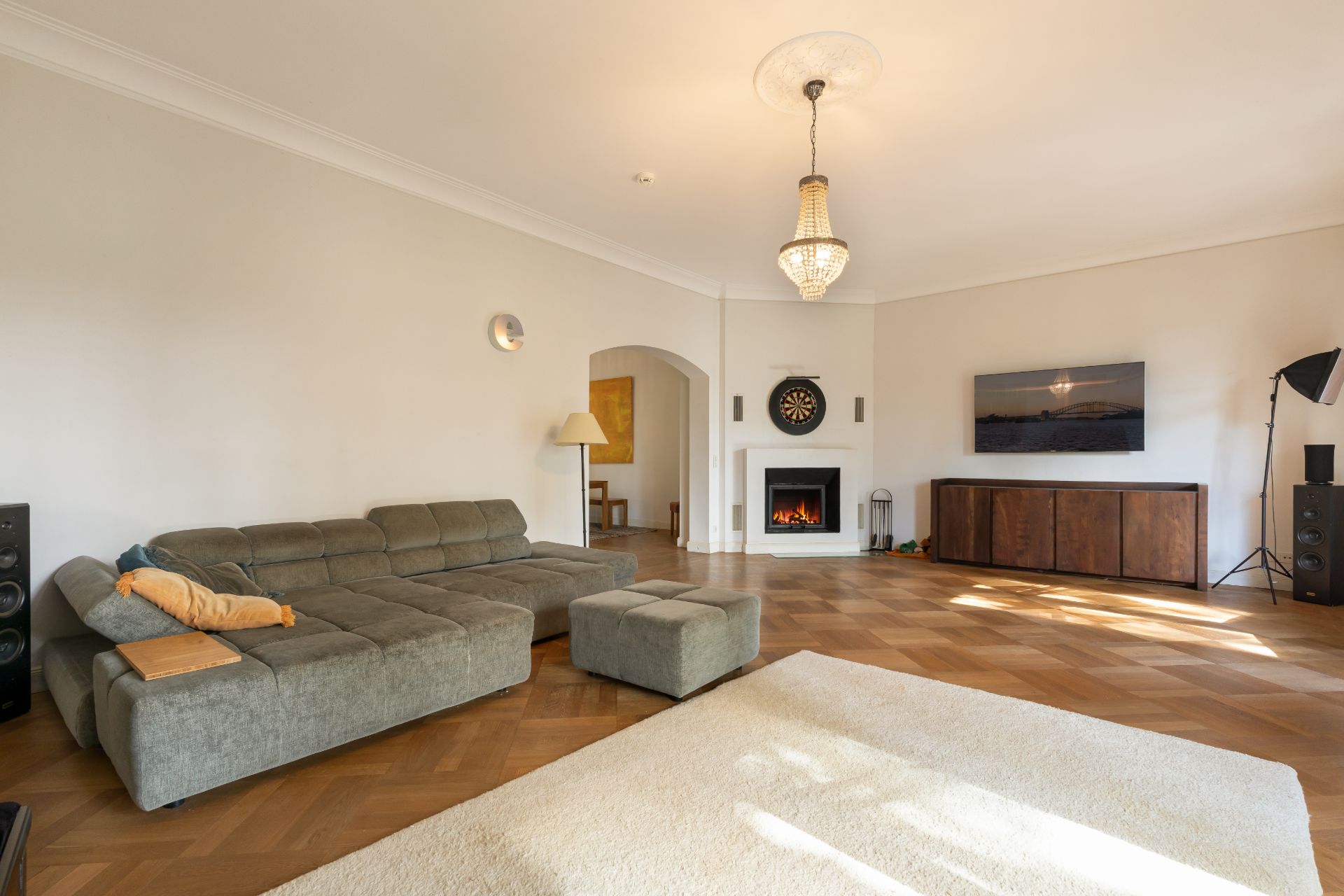 Helles Wohnzimmer mit grauem Sofa, Kamin, rundem Teppich und TV an der Wand.