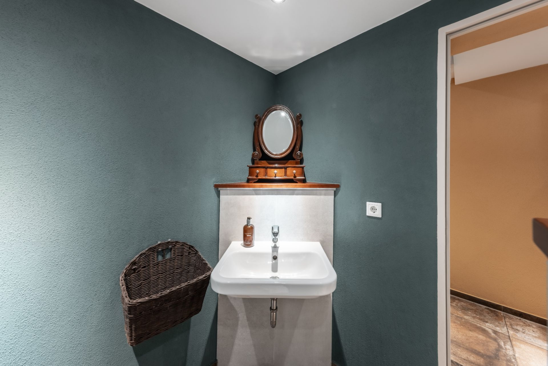 Kleines Badezimmer mit Waschbecken, Wandspiegel und einem Korb an der Wand.