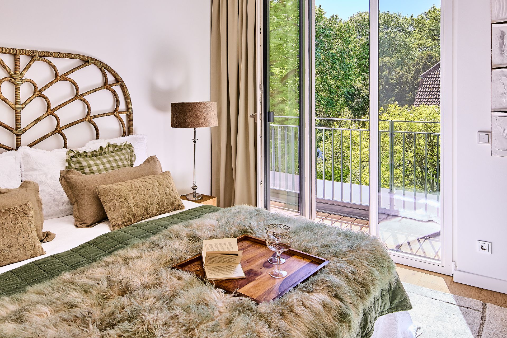 Schlafzimmer mit Doppelbett, Stehlampe und Zugang zu einem Balkon mit Ausblick ins Grüne.
