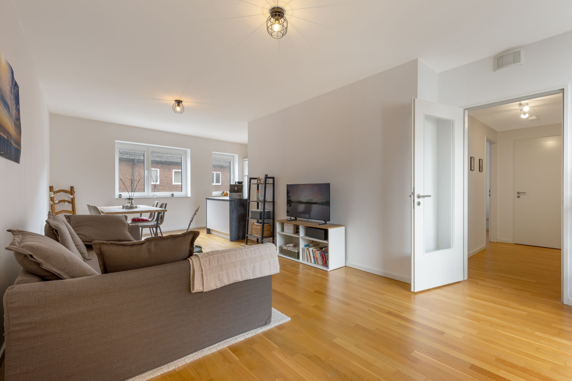 Helles Wohnzimmer mit Sofa, Fernseher, Essbereich und Holzboden.