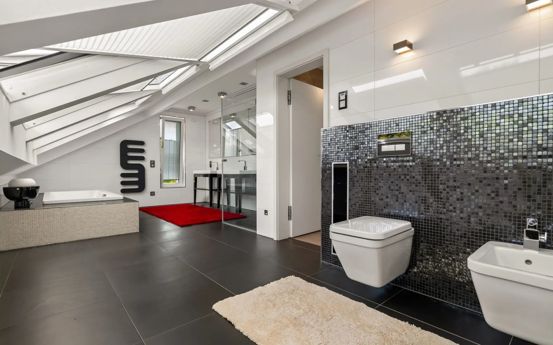 Modernes Badezimmer mit Badewanne, WC, Bidet, großem Fenster und schwarzen Fliesen.