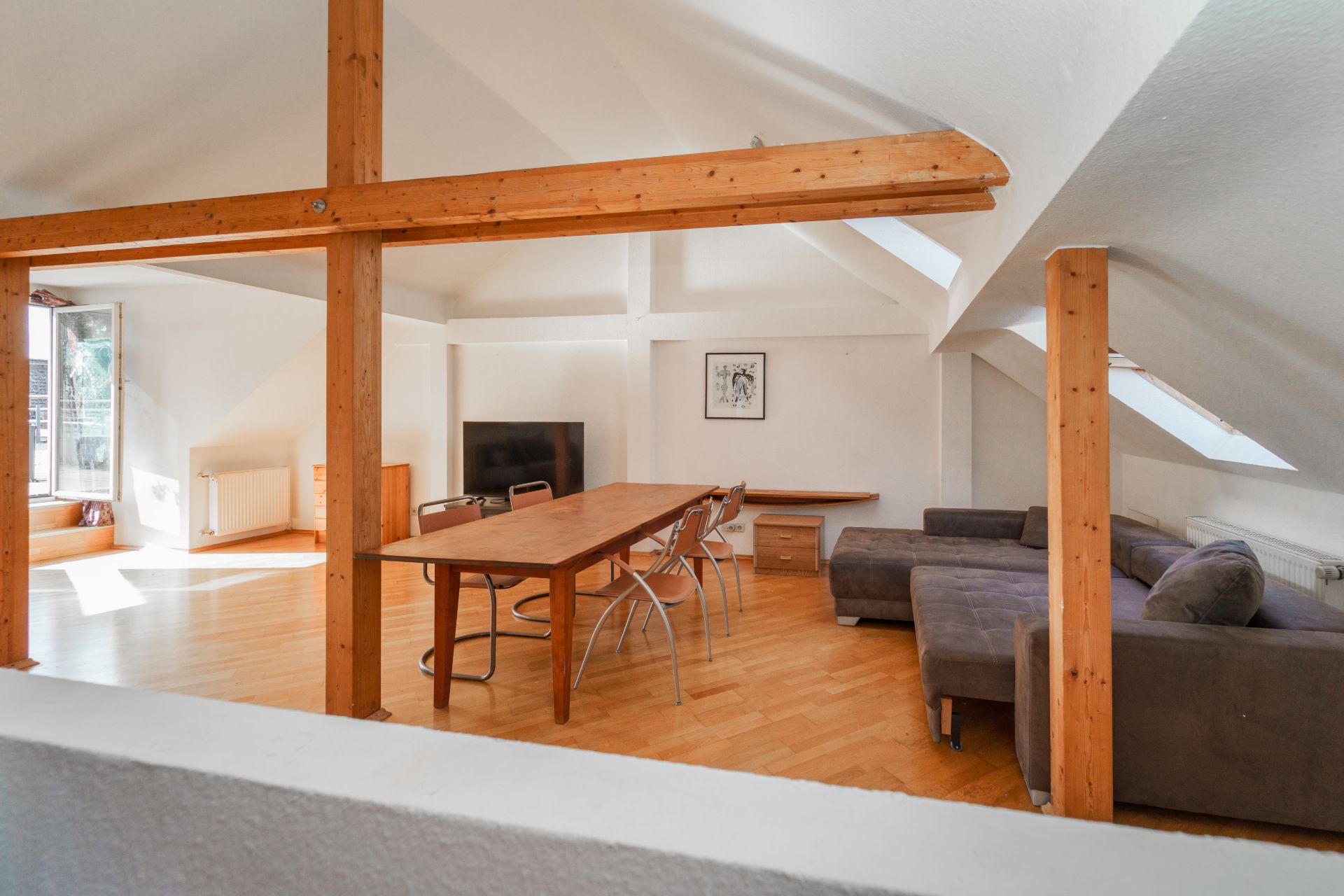 Wohnzimmer mit Holzbalken, Esstisch, Stühlen, Sofa und Fernseher unter Dachschrägen.