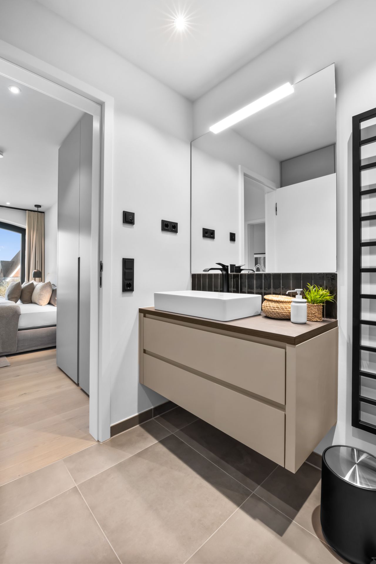 Modernes Badezimmer mit Waschbecken, großem Spiegel und Blick ins Schlafzimmer.
