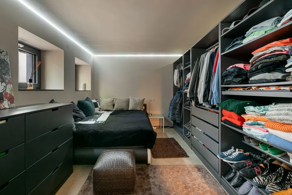 Modernes Schlafzimmer mit offenem Kleiderschrank, Doppelbett, Kommode und Fenster.