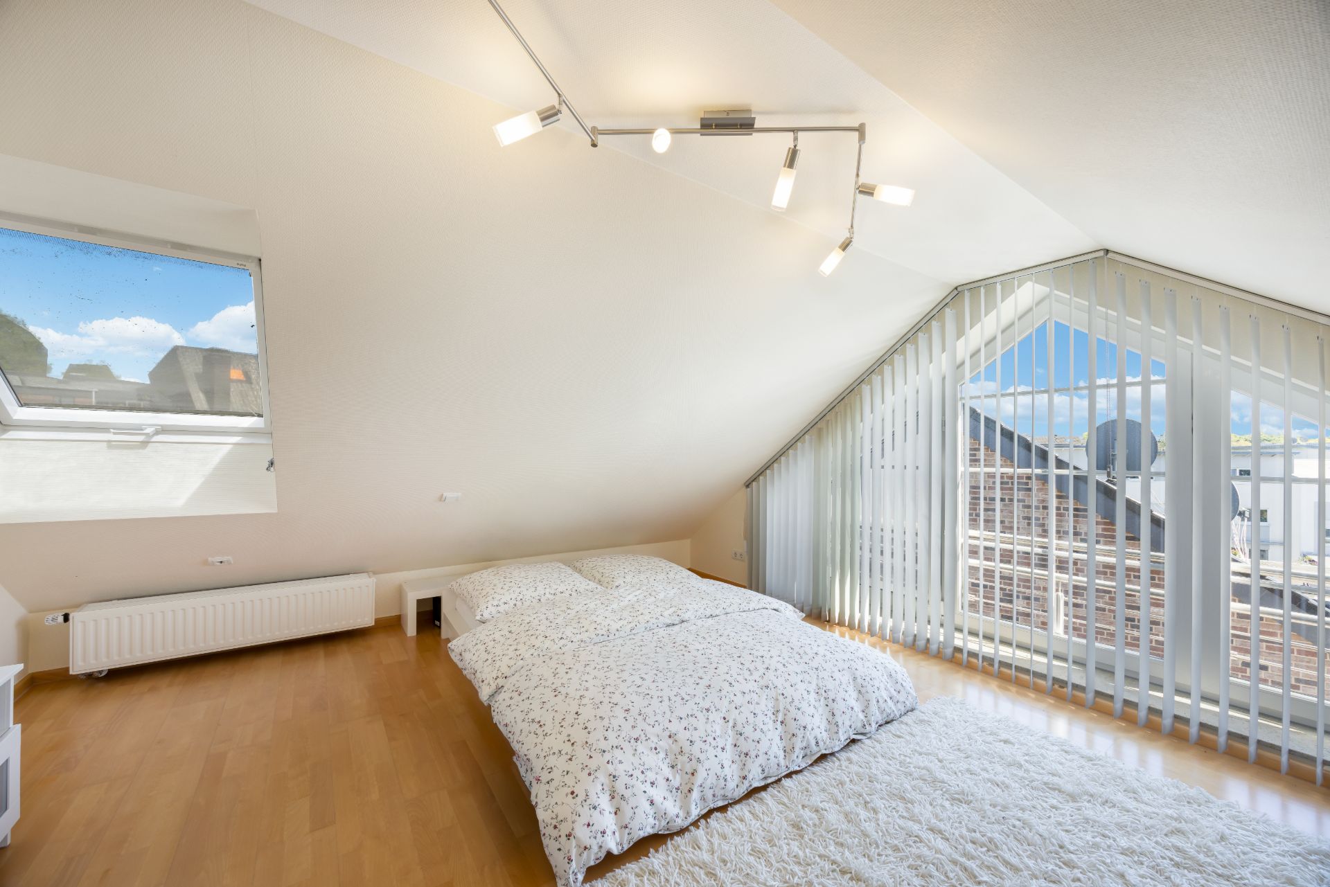 Helles Schlafzimmer mit Doppelbett, Parkettboden und großen Fenstern unter dem Dach.