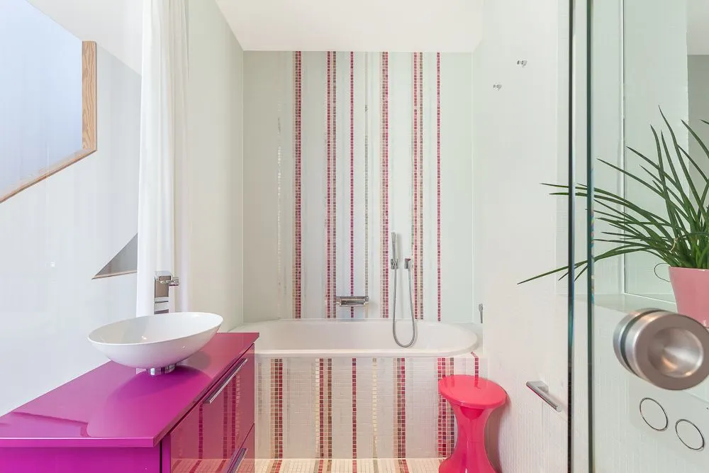 Modernes Bad mit Badewanne, pinkem Waschbeckenunterschrank, Pflanzen und gestreifter Wand.