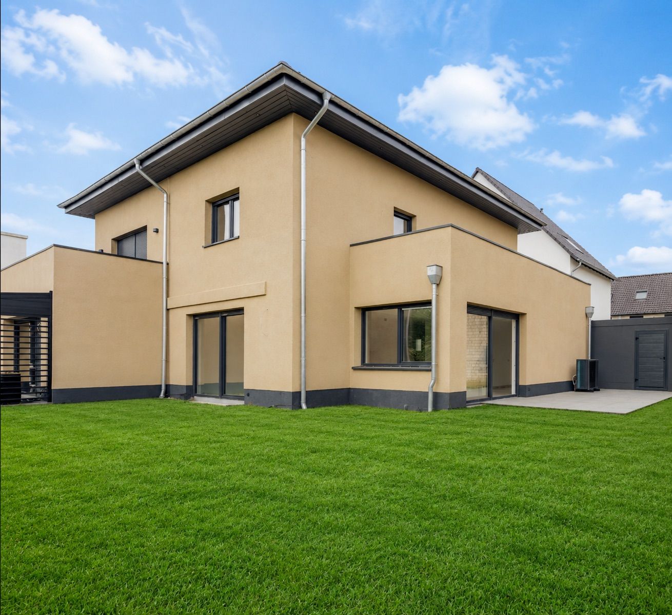 Modernes, zweistöckiges Wohnhaus mit beige Fassade und großem Garten unter blauem Himmel.