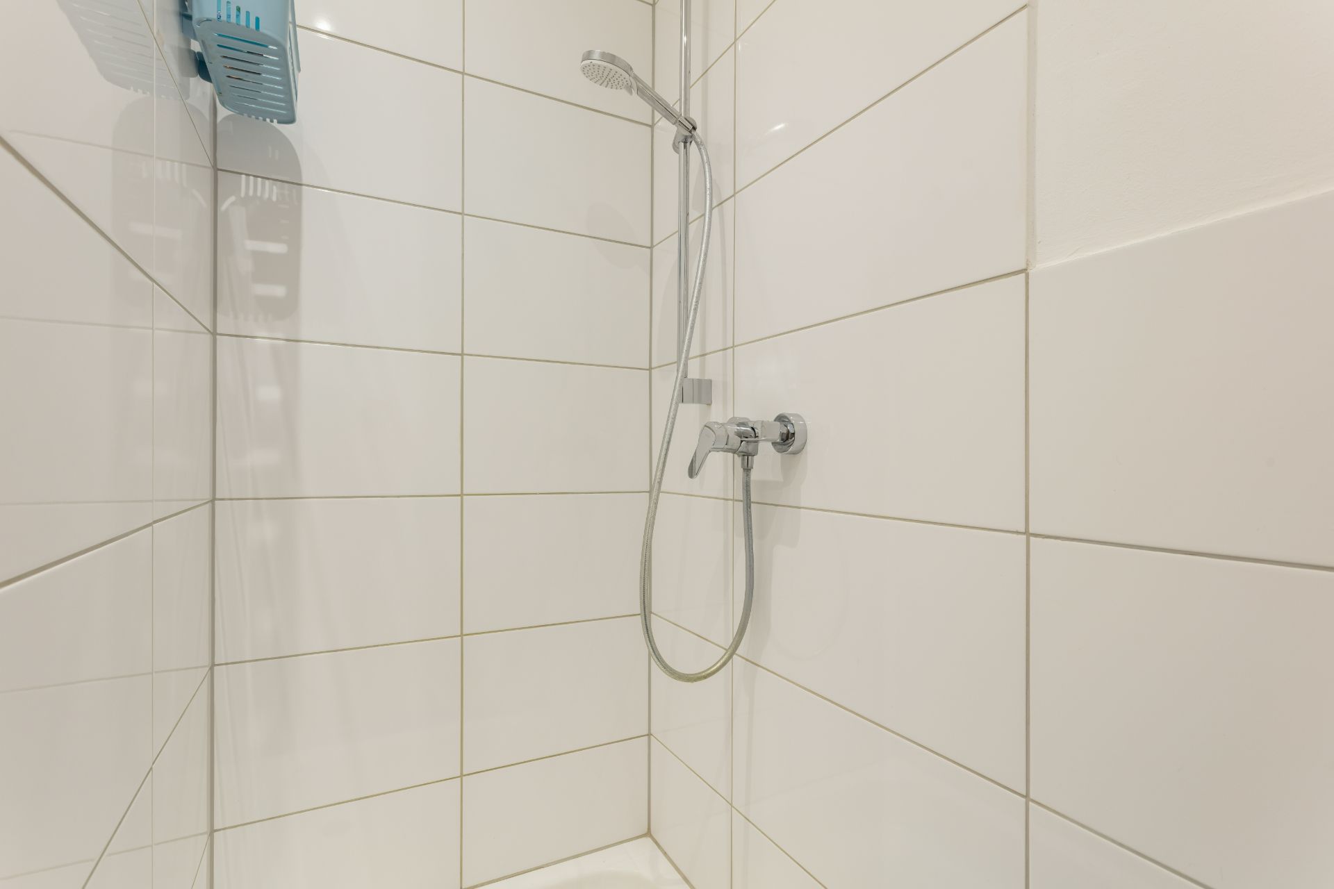 Dusche mit weißen Fliesen, Duschkopf und Seifenablage an der Wand.