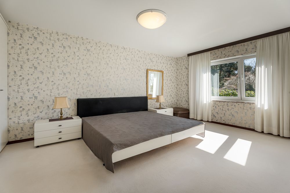 Helles Schlafzimmer mit Doppelbett, zwei Nachttischen, Lampe und großem Fenster mit Vorhängen.