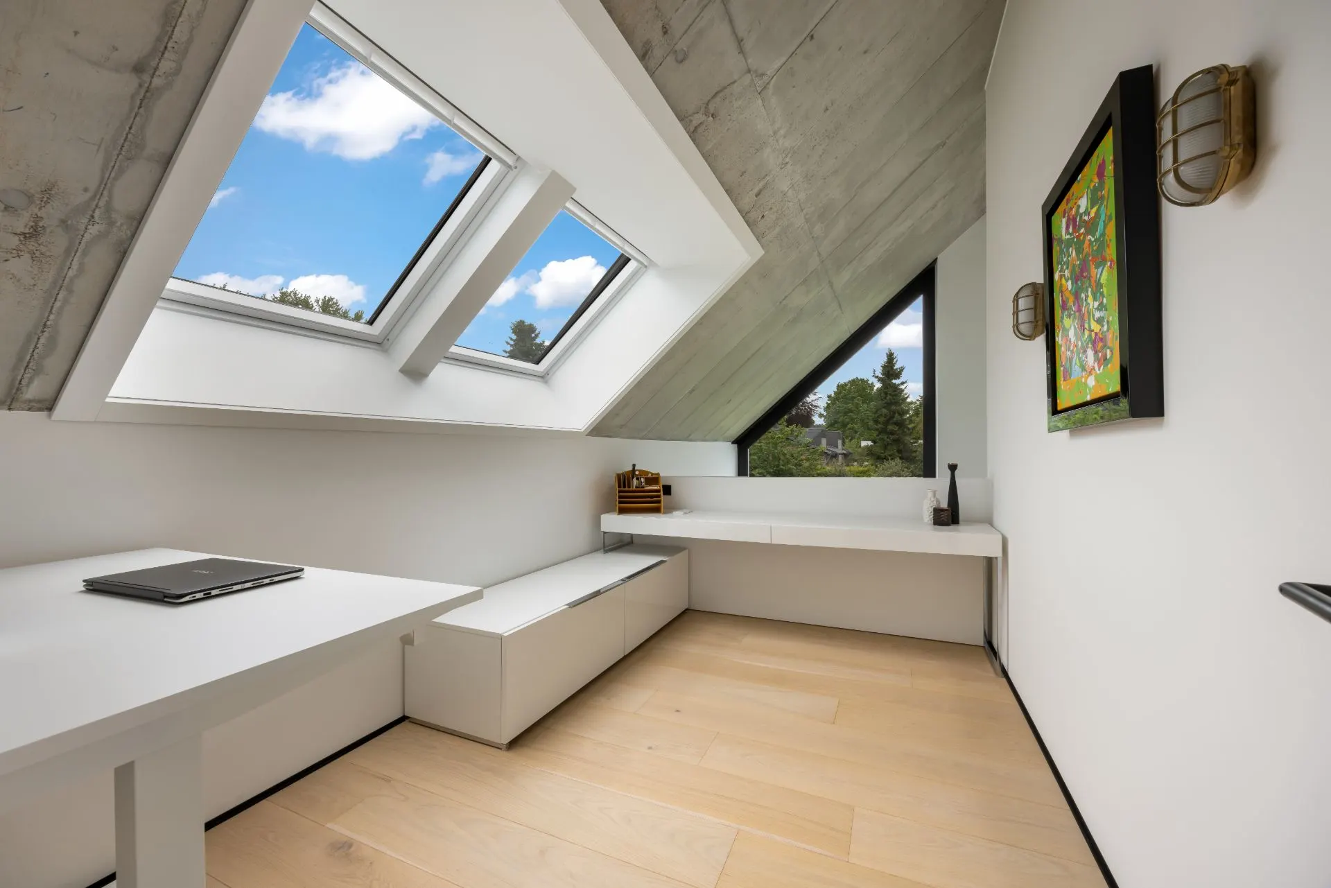 Heller Raum mit Schreibtisch, Dachfenstern, Holzfußboden und Bild an der Wand.