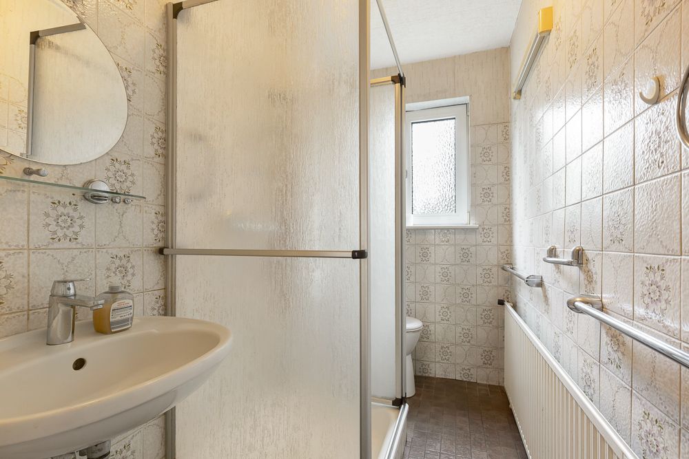 Kleines Badezimmer mit Dusche, Waschbecken, Fenster und gemusterten Fliesen an den Wänden.