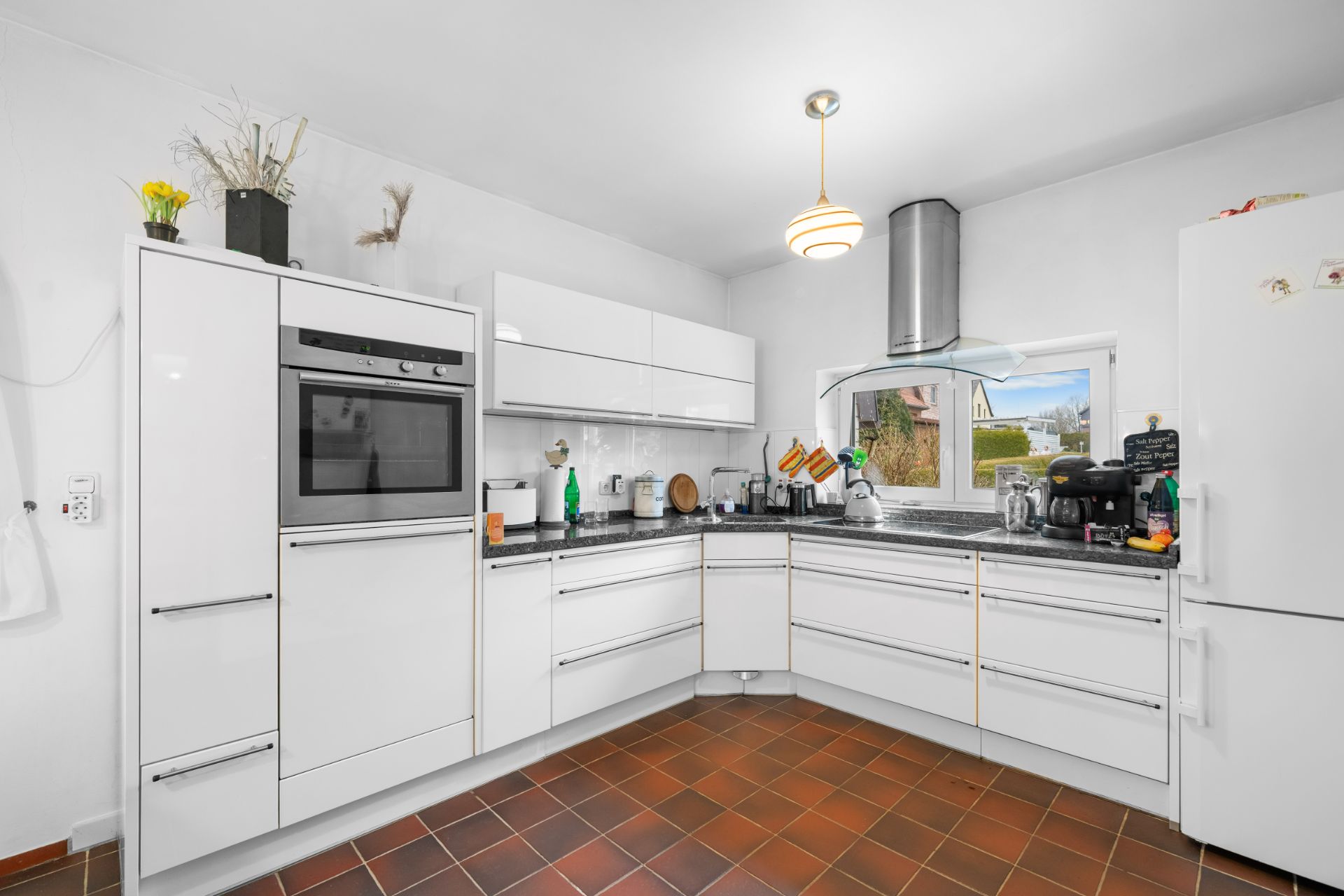 Moderne weiße Küche mit Einbaugeräten, Eckspüle und braunem Fliesenboden.