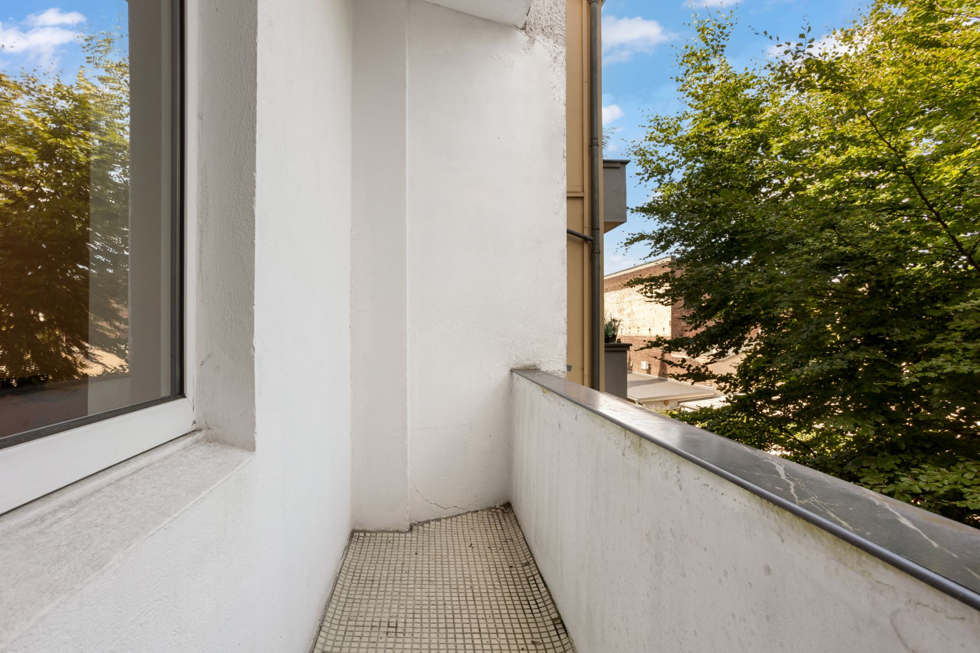 Schmaler Balkon mit weißer Wand und Ausblick auf Bäume.