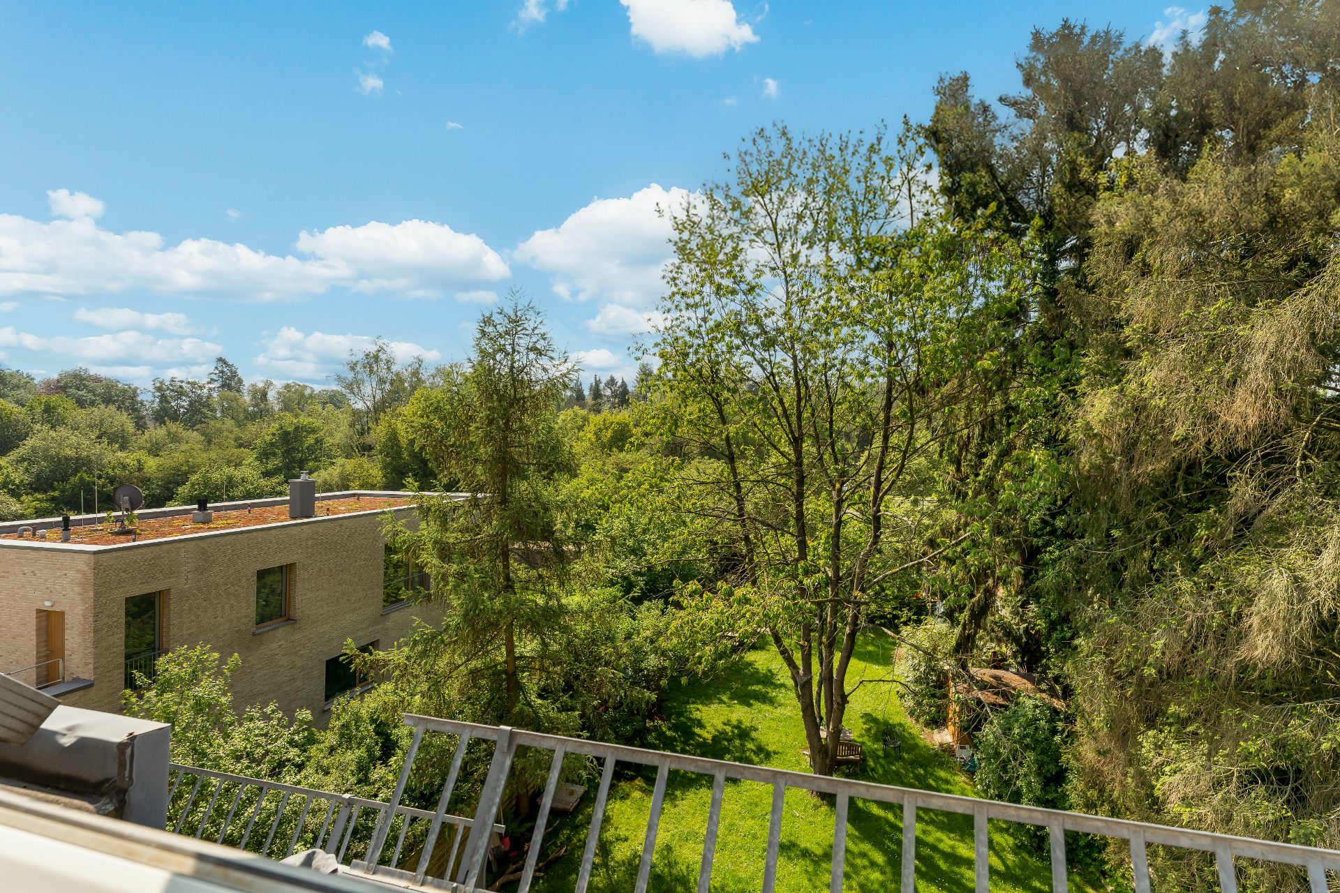 Blick auf grünen Garten mit Bäumen und modernes Wohngebäude im Hintergrund.