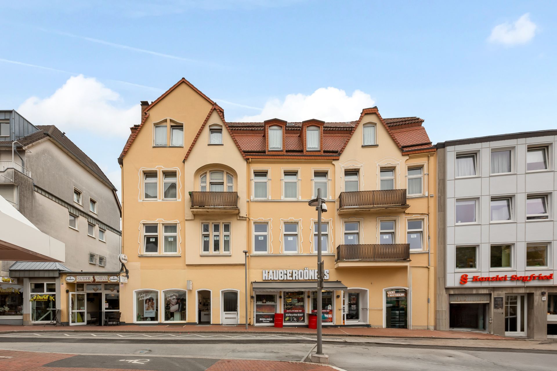 Mehrstöckiges Wohngebäude mit gelber Fassade und Balkonen, Geschäfte im Erdgeschoss.