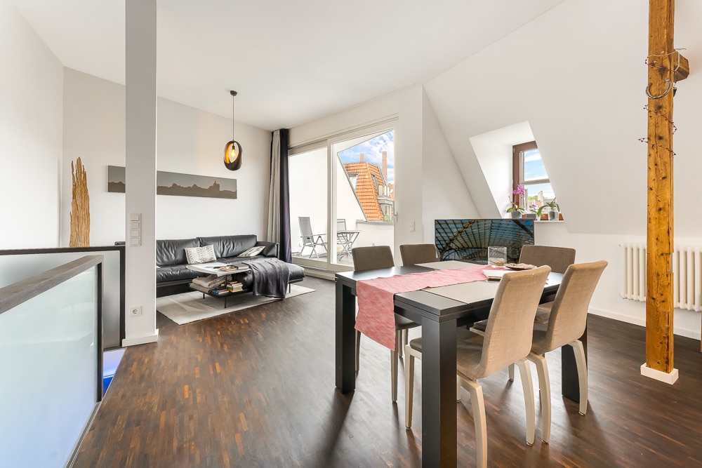 Helles Wohnzimmer mit Essbereich, Holzboden, Sofa, Esstisch und Zugang zu einem Balkon.