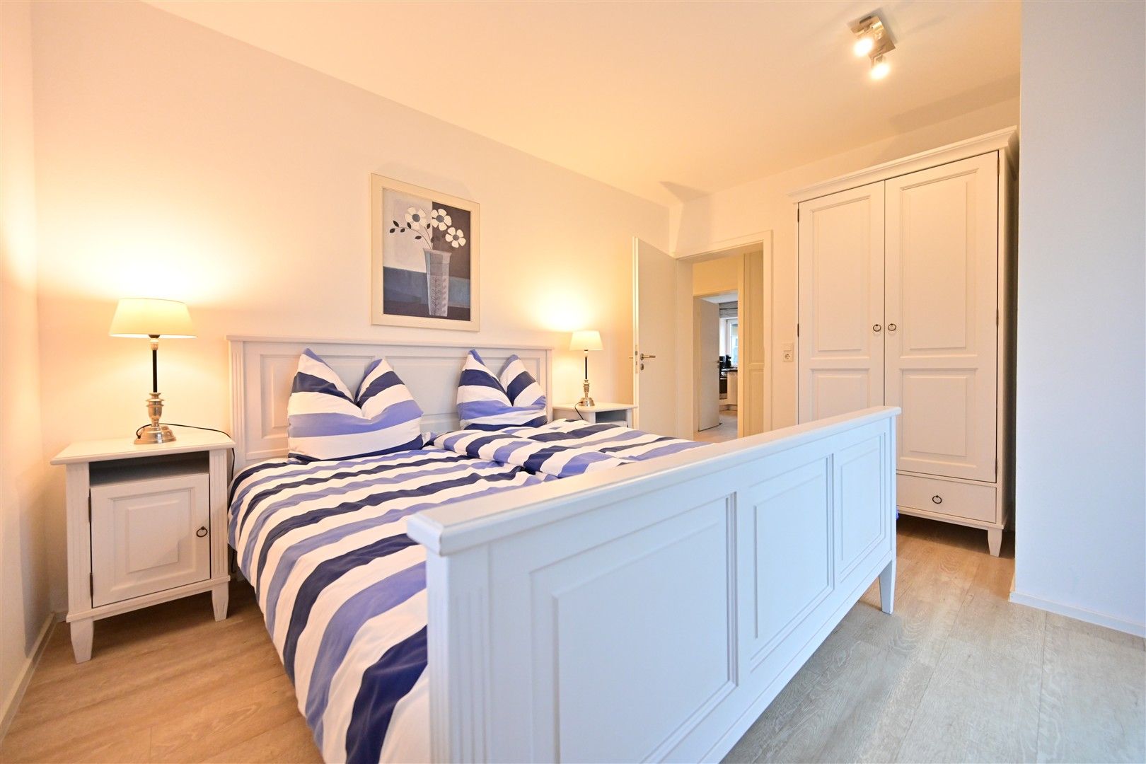 Helles Schlafzimmer mit Doppelbett, weißen Möbeln, zwei Nachttischen und Kleiderschrank.