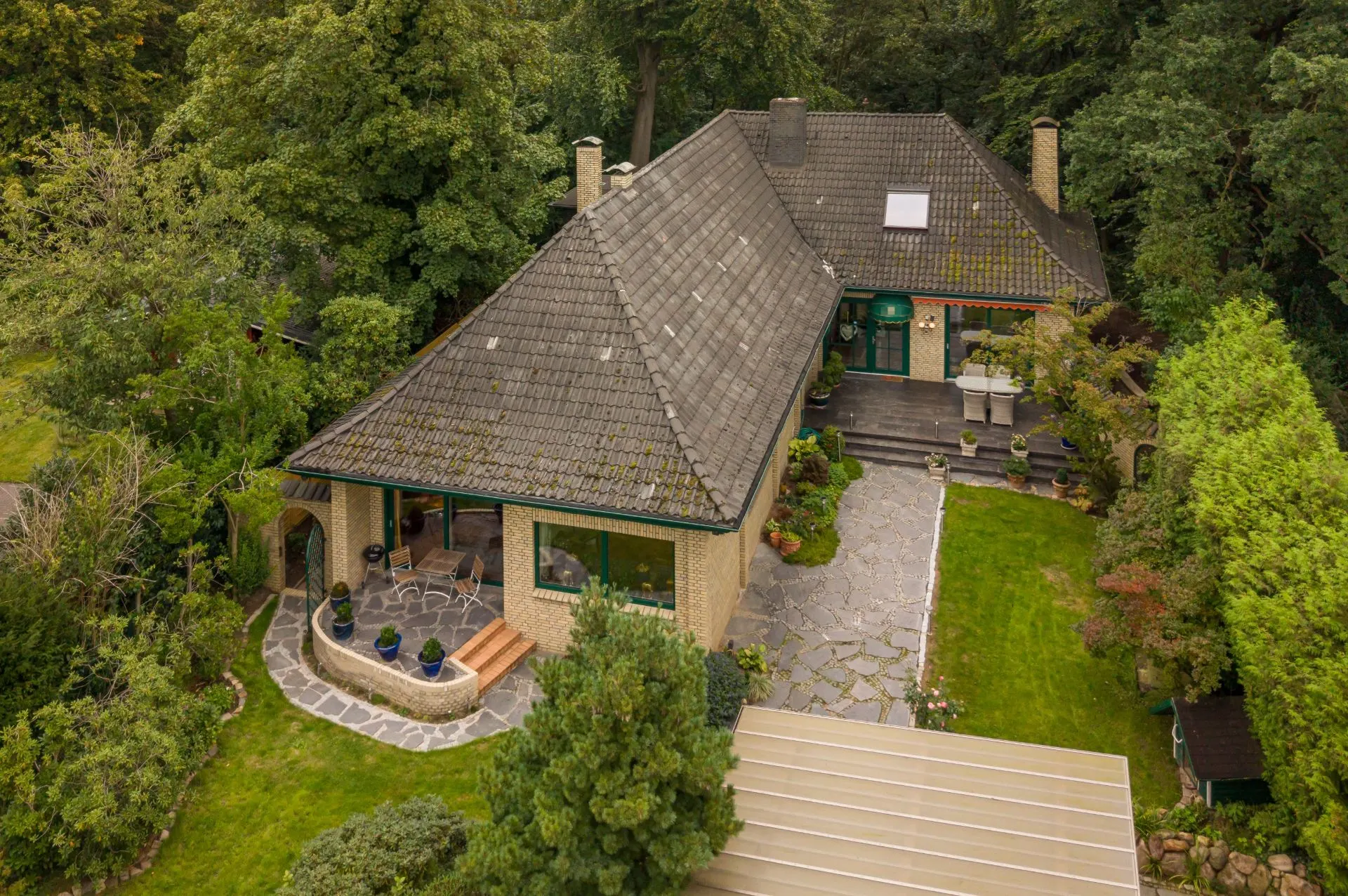 Luftaufnahme eines Einfamilienhauses mit Garten, Terrasse und viel umgebendem Grün.