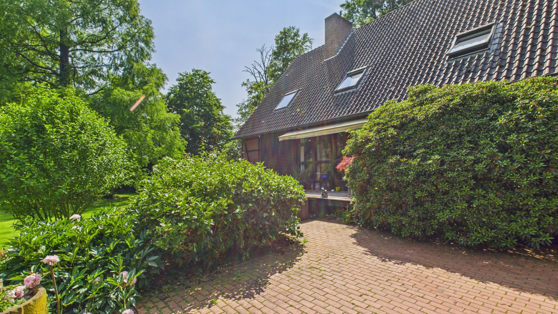 Außenansicht eines Hauses mit Ziegeldach, Terrasse und viel Grün rundherum.