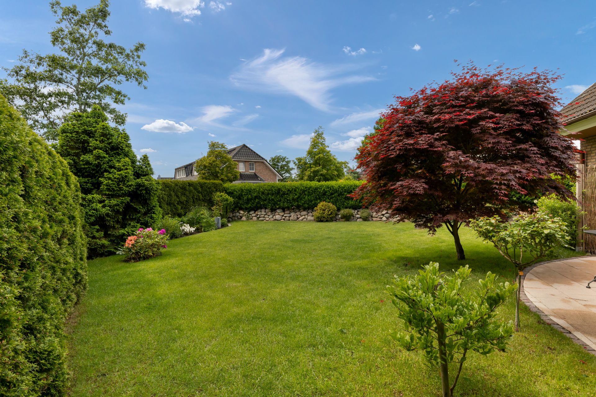 Garten mit grünem Rasen, Bäumen und Büschen unter blauem Himmel.