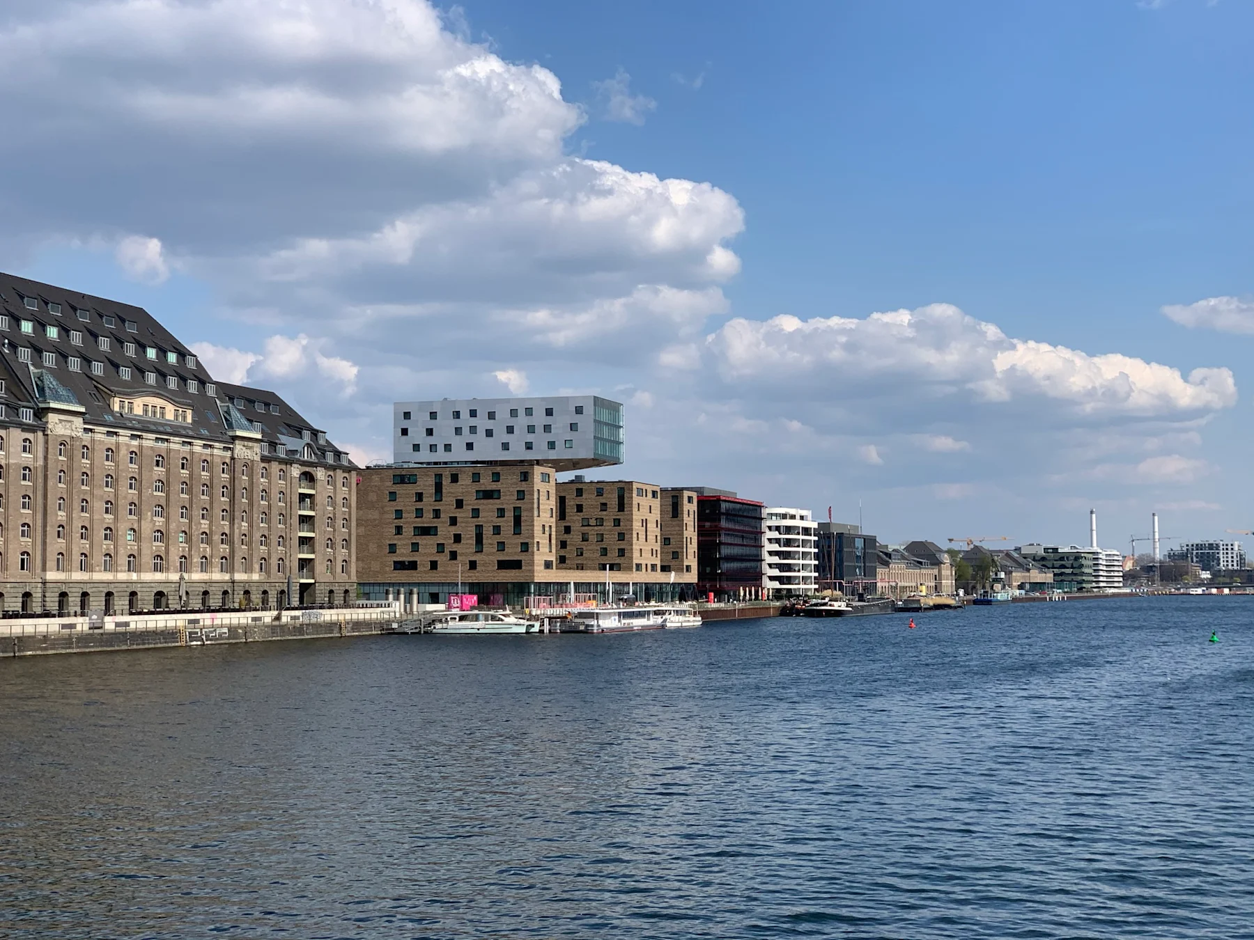 Wasserfront mit modernen und historischen Gebäuden am Ufer unter blauem Himmel.