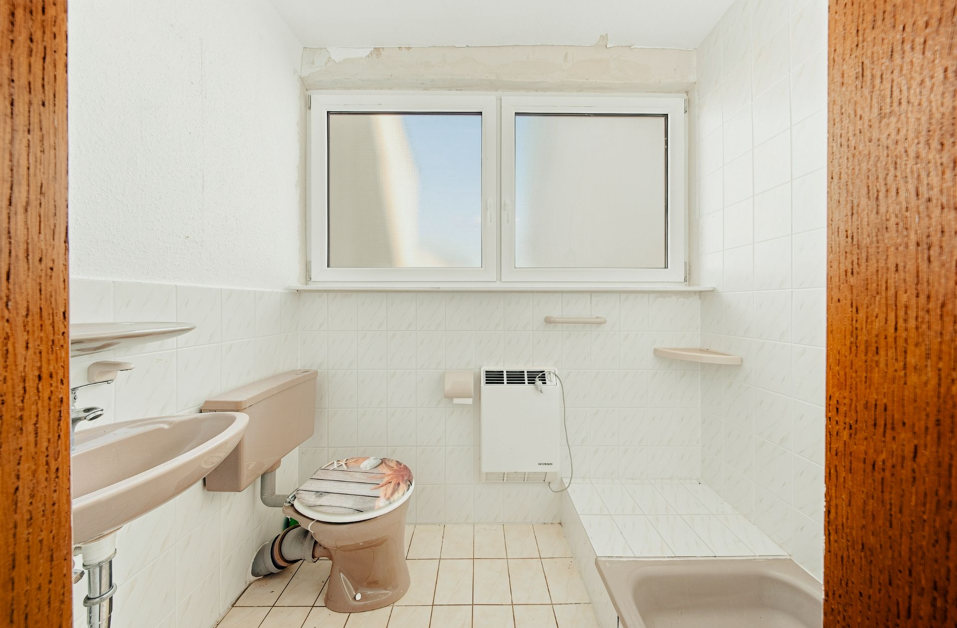 Helles Bad mit WC, Waschbecken, Fenster und Dusche, beigefarbene Sanitäranlagen.