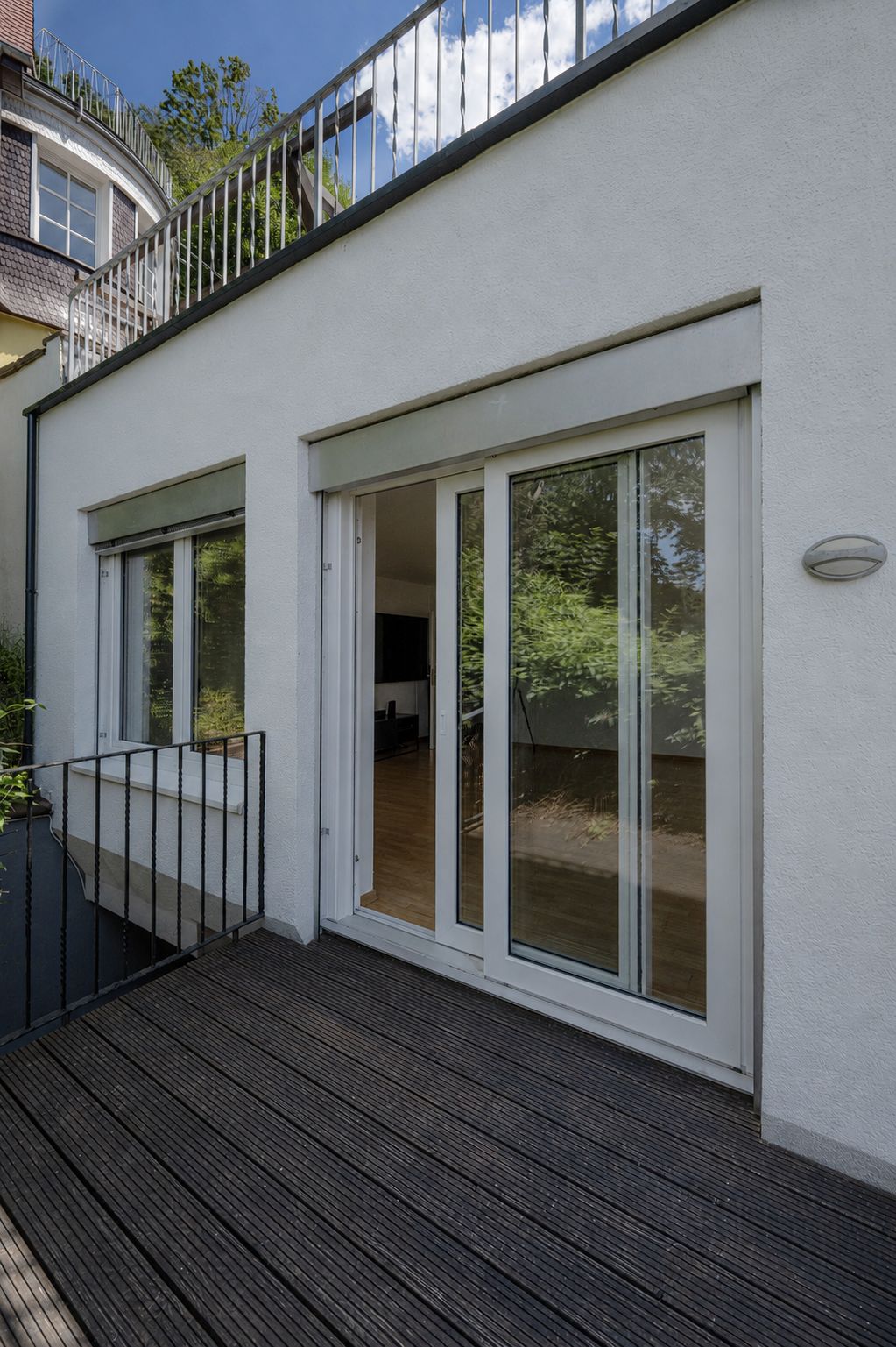 Terrasse mit Holzdielen und Zugang durch Schiebetüren zu einem hellen Innenraum.