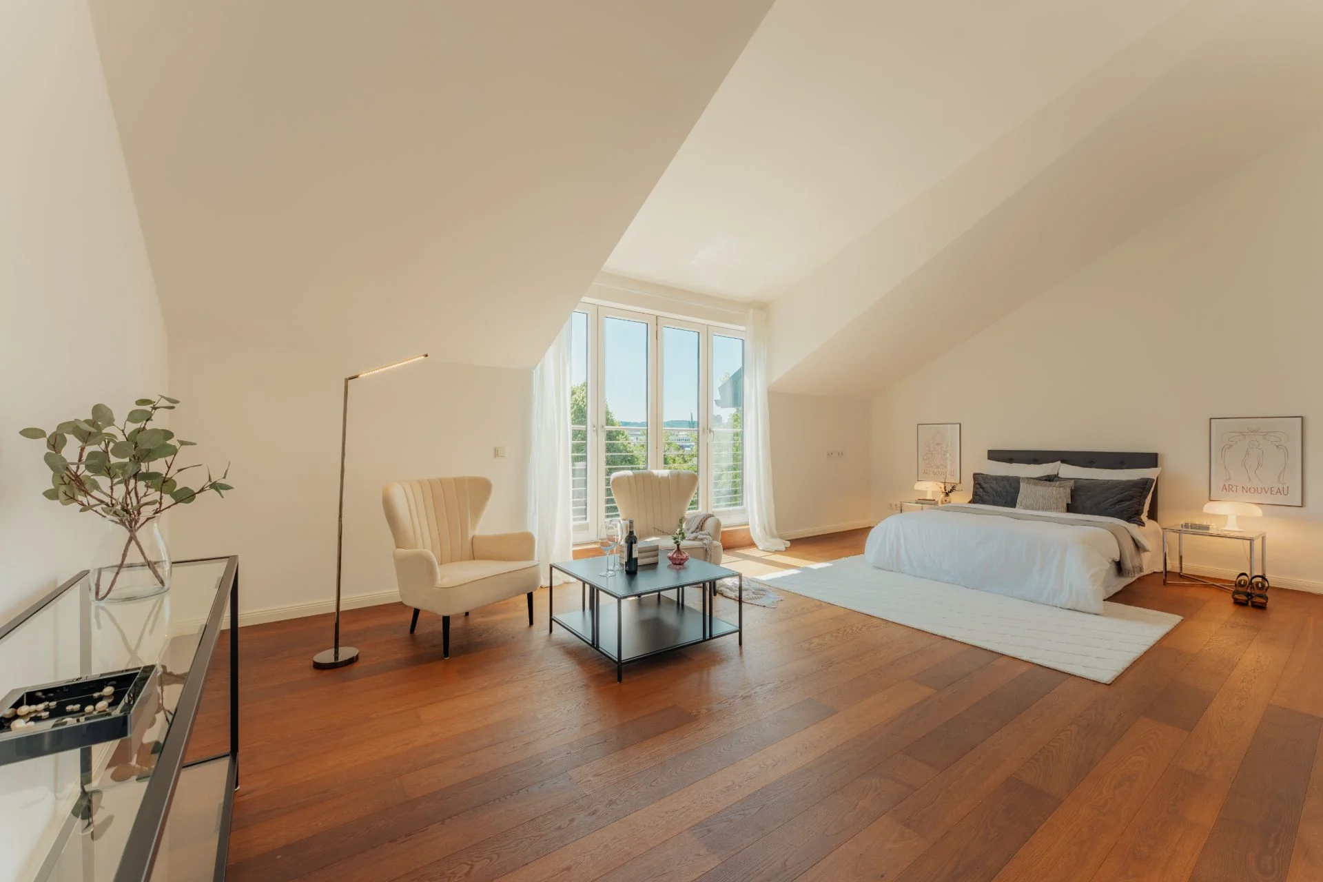 Helles Schlafzimmer mit Holzboden, Doppelbett, zwei Sesseln und großen Fenstern.