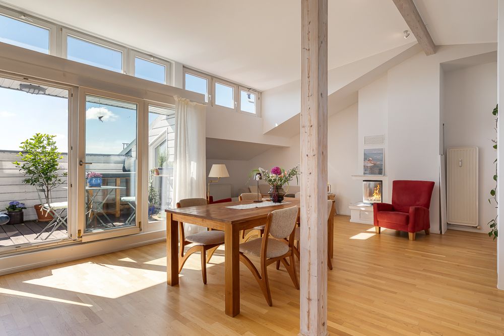 Helles Wohnzimmer mit Holzboden, Esstisch, rotem Sessel und Zugang zu einem Balkon mit Pflanzen.