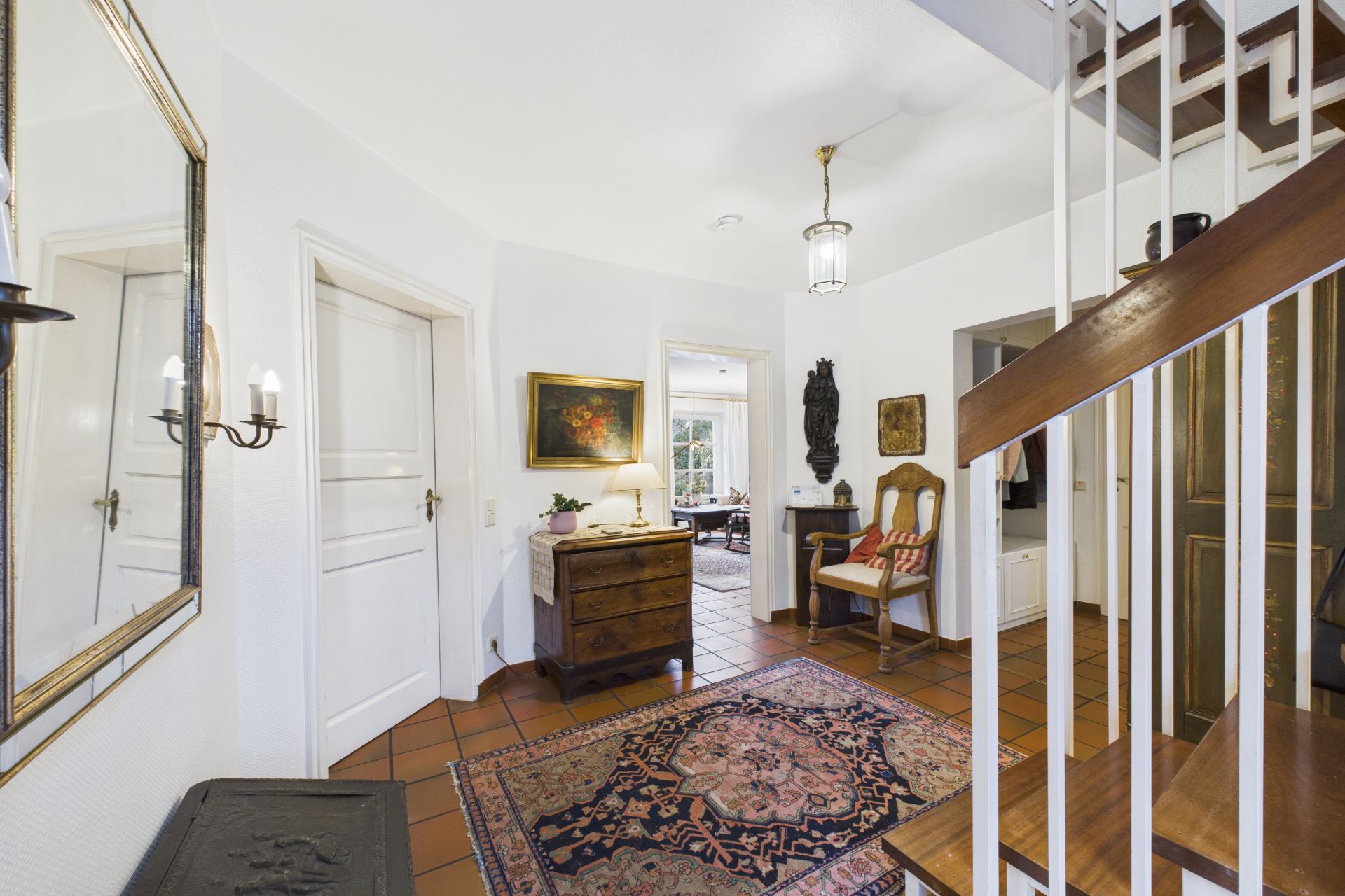 Flur mit Teppich, Holztreppe, Kommode, Stuhl und Wanddekoration in einem Wohnhaus.