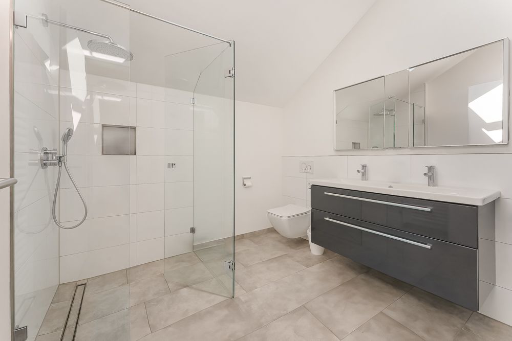 Modernes Badezimmer mit großer Glasdusche, Doppelwaschbecken, Spiegel und Hänge-WC.