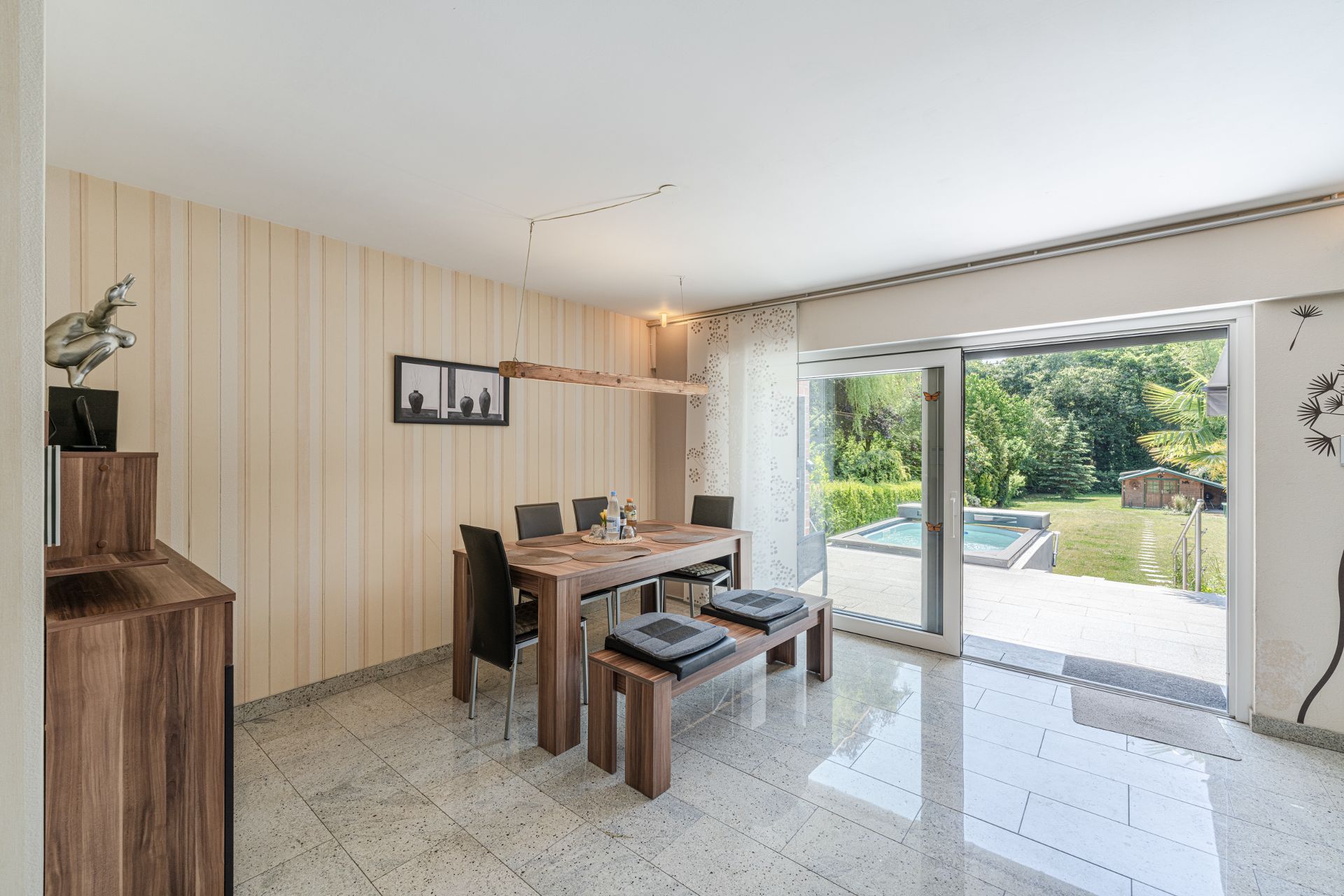 Essbereich mit Holztisch, Stühlen und Bank, große Fensterfront mit Blick auf Garten und Pool.