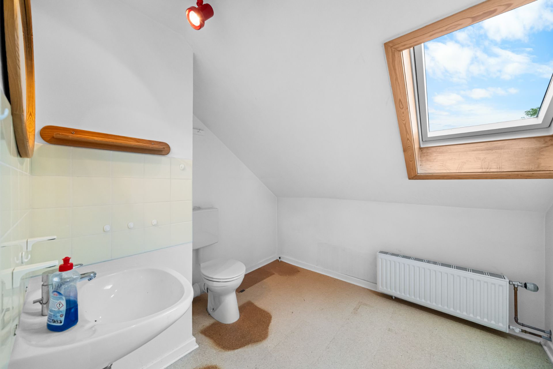 Helles Badezimmer mit Waschbecken, Toilette, Heizkörper und Dachfenster.