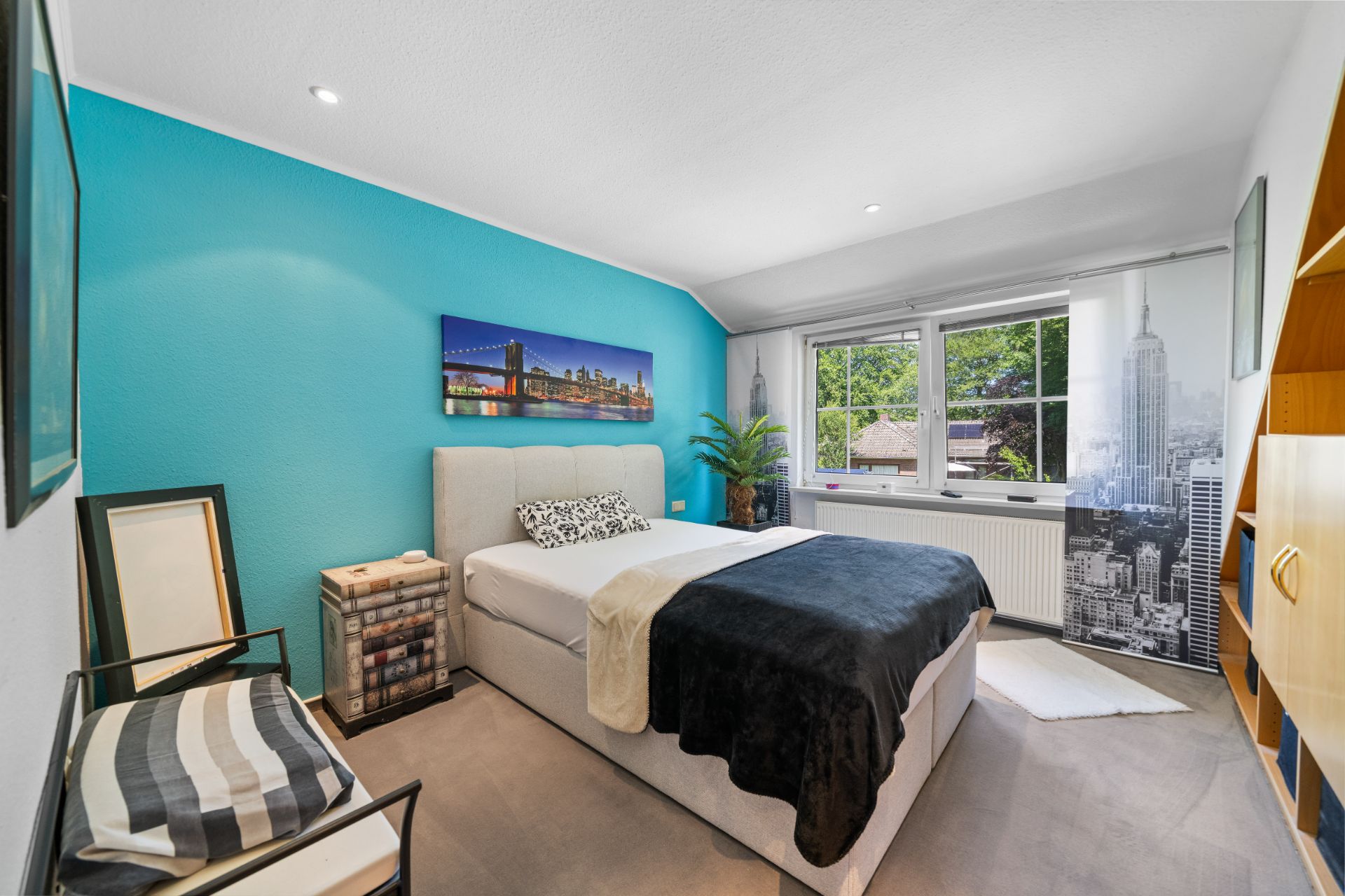 Modernes Schlafzimmer mit Doppelbett, großem Fenster und türkiser Akzentwand.