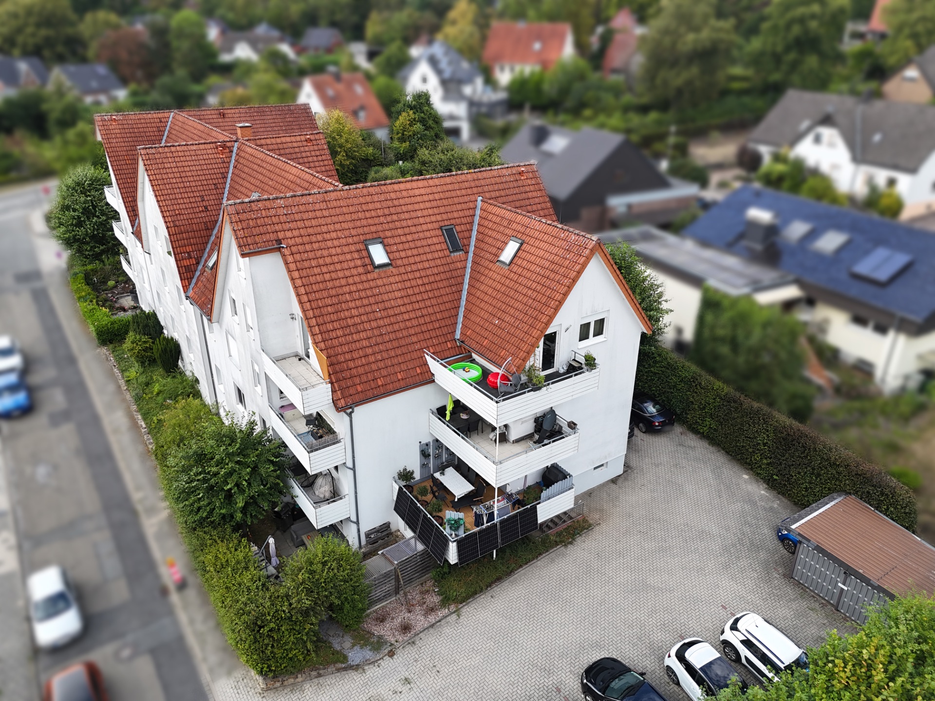 Mehrfamilienhaus mit roten Dächern, Balkonen und angrenzendem Parkplatz, von oben fotografiert.