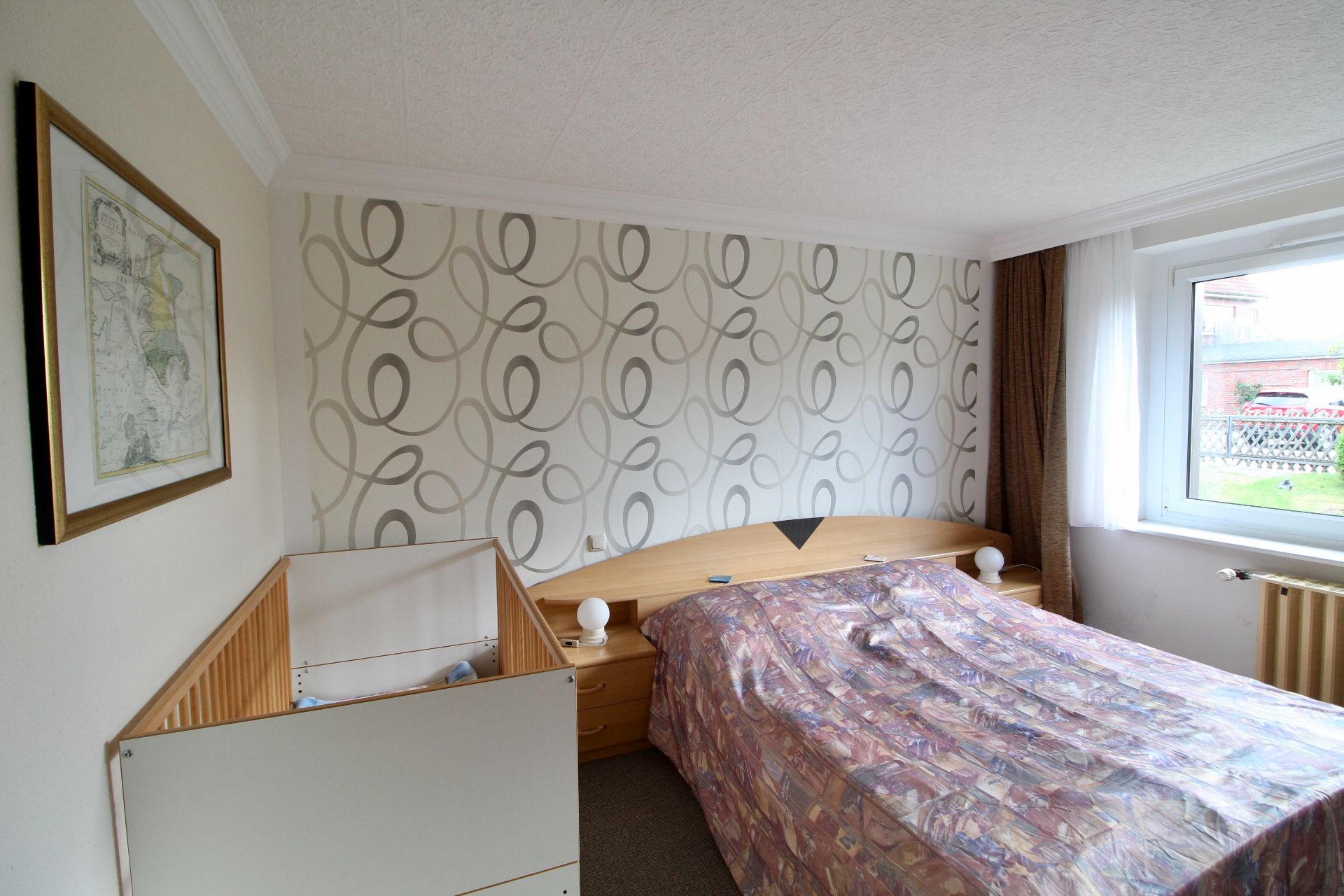Schlafzimmer mit einem Doppelbett, einem Babybett, Nachttischen und großem Fenster.