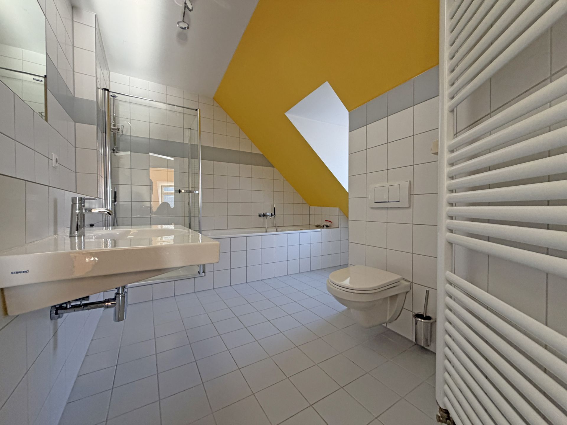 Modernes Badezimmer mit Badewanne, Waschbecken, WC und gelber Schräge.