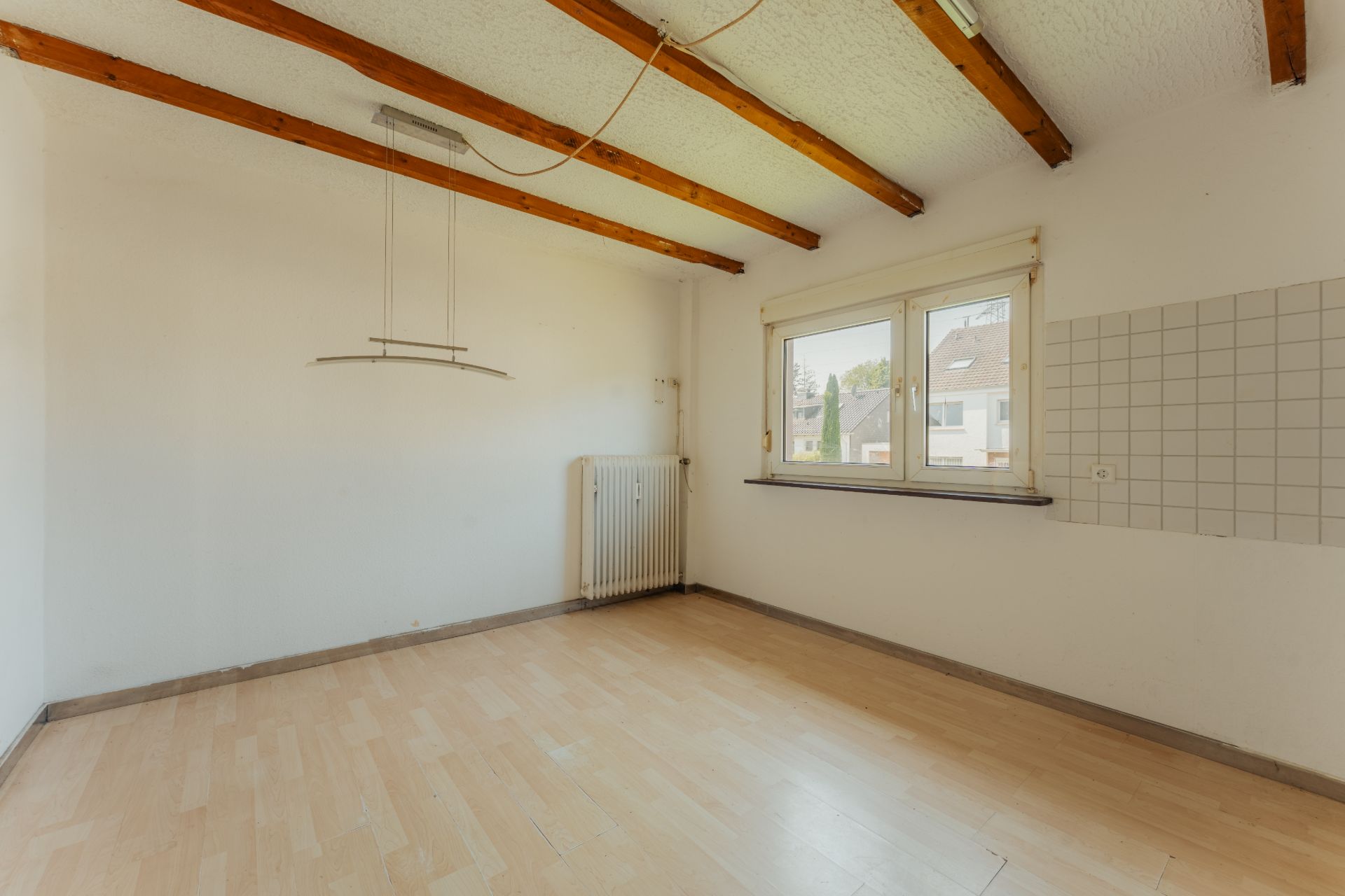 Leerer Raum mit Holzbalkendecke, Fenster, Heizung und Fliesen an einer Wand.