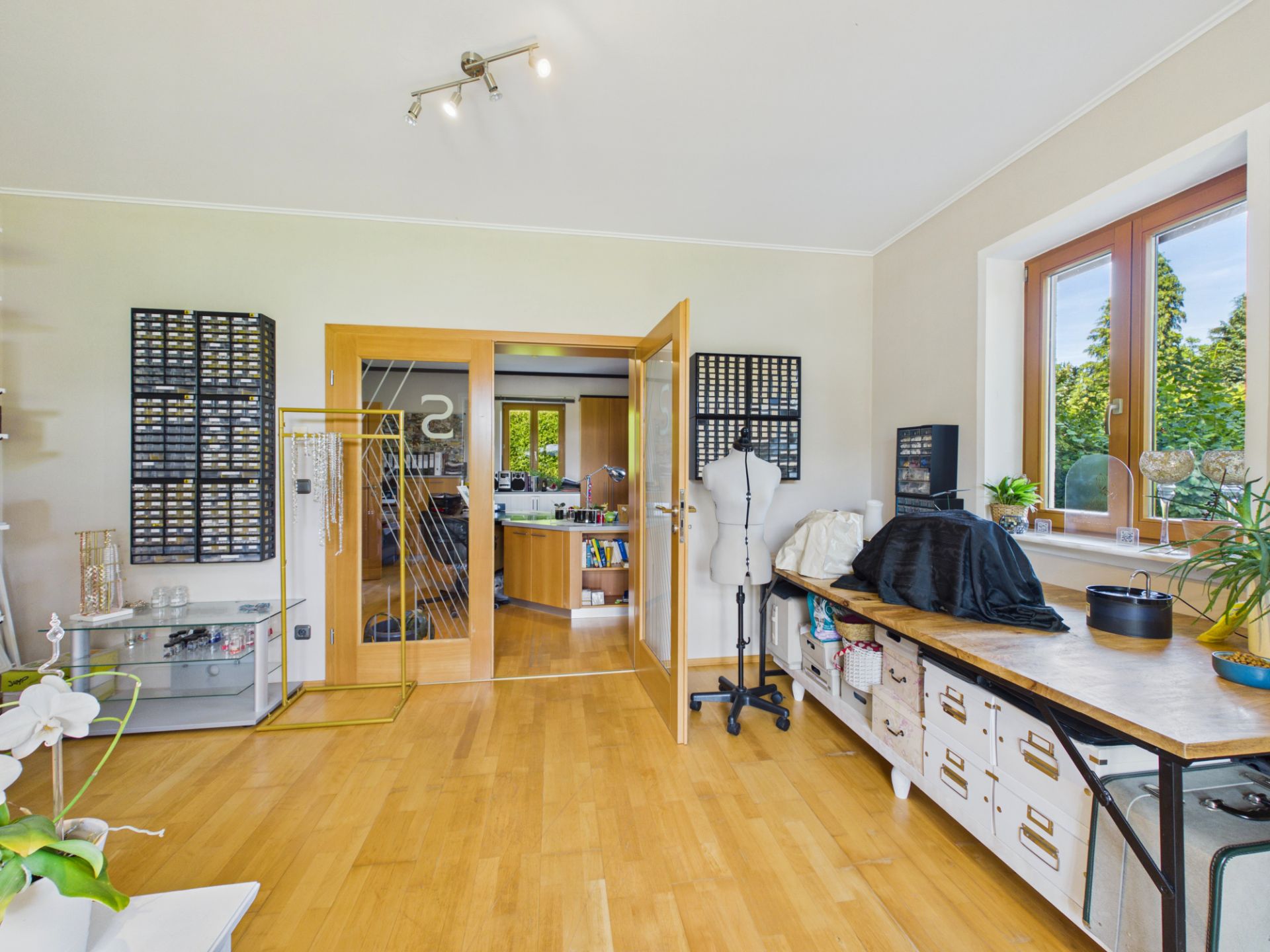 Helles Arbeitszimmer mit Holzfußboden, Schreibtisch, Schneiderpuppe und Blick ins Nebenzimmer.