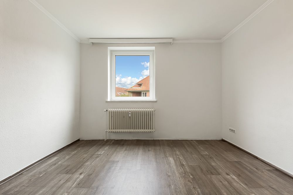 Leeres Zimmer mit weißem Wänden, Fenster und Heizkörper, brauner Holzboden.
