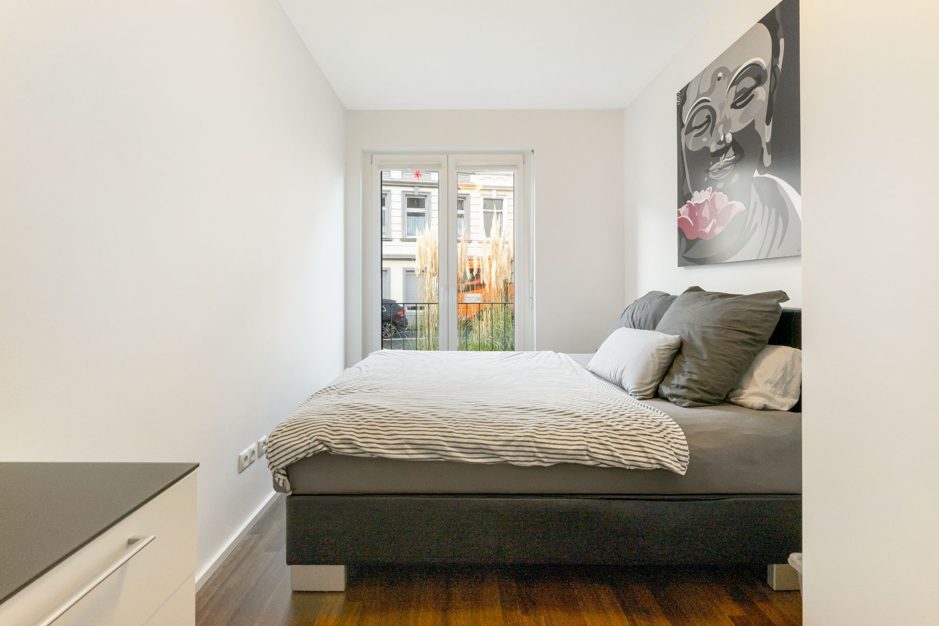 Helles Schlafzimmer mit Doppelbett, großem Fenster und Bild an der Wand.