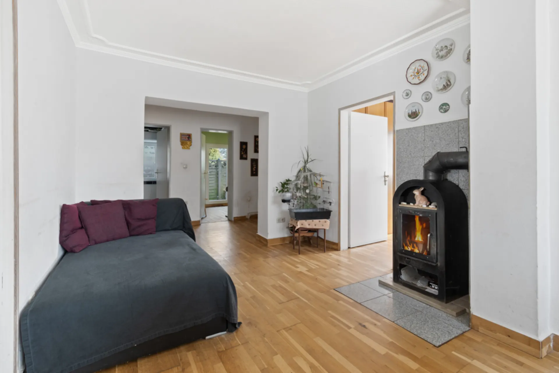 Wohnzimmer mit Holzofen, Sofa, Holzboden und dekorativen Tellern an der Wand.