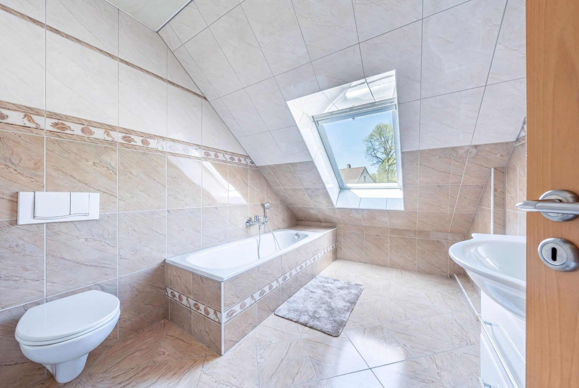 Helles Badezimmer mit Badewanne, WC, Waschbecken und großem Dachfenster.