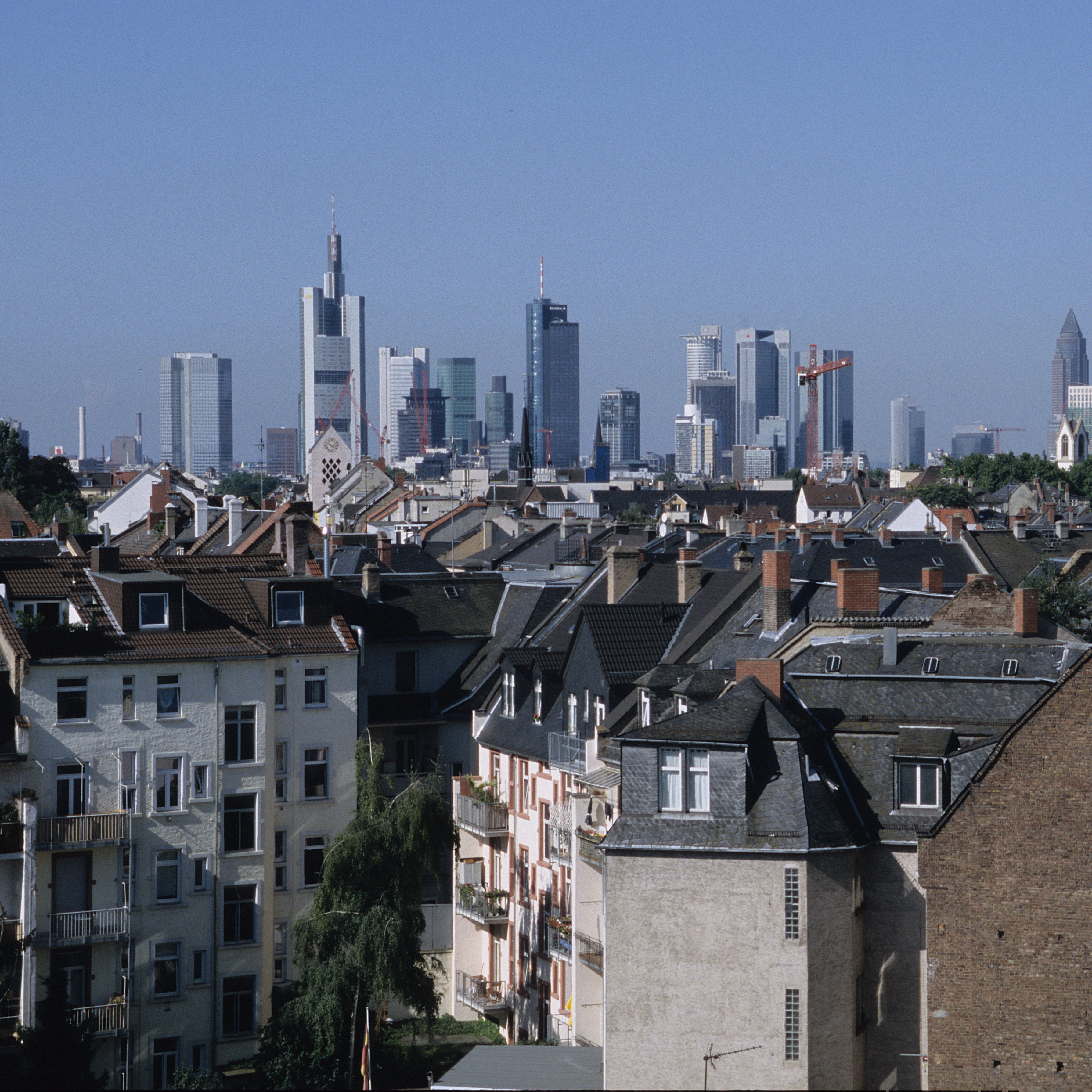 Blick über Wohnhäuser mit moderner Skyline im Hintergrund bei klarem Himmel.